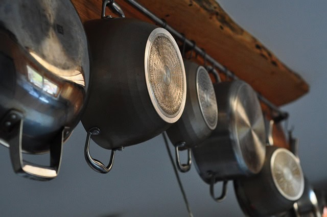 Several metallic pots hang from a wooden rack in a kitchen setting, creating an organized and functional display against a neutral background.